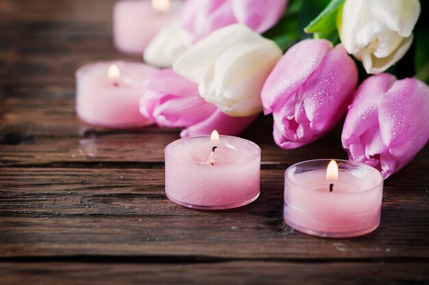 Pink and white tulips and candles on the wooden table