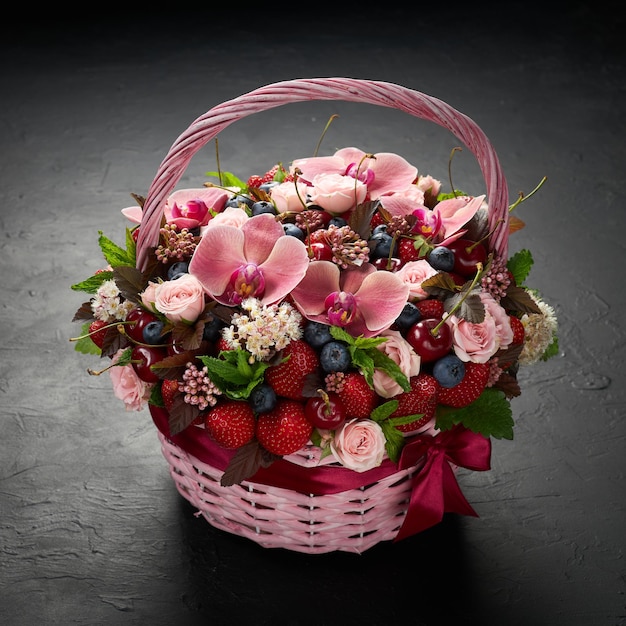 黒の背景にイチゴブルーベリーチェリーとピンクの花で満たされたピンクの籐のバスケット