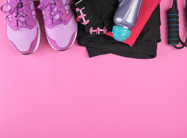 Pink women's sneakers, bottle of water, gloves and a jump rope for sports 