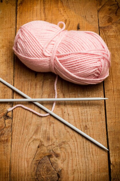 Pink wool skein and needles on a wooden table