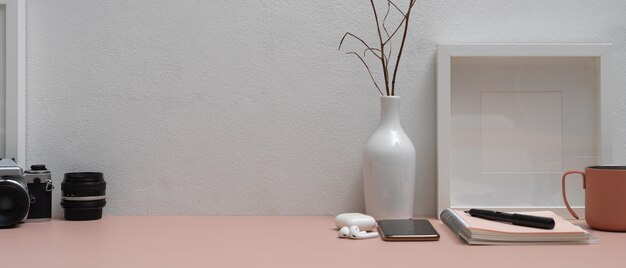 Pink worktable with stationery, smartphone, camera, accessories, decorations and copy space