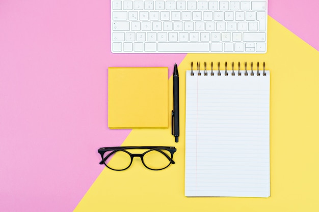 Pink and yellow layout, notepad, writing, keyboard and glasses