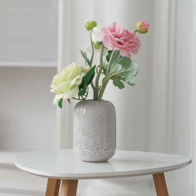 Pink and yellow roses in modern white vase on white side table