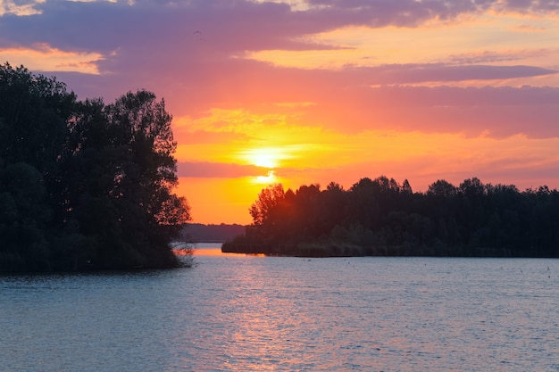 Розово-желтый закат и отражение солнца на поверхности воды озера.