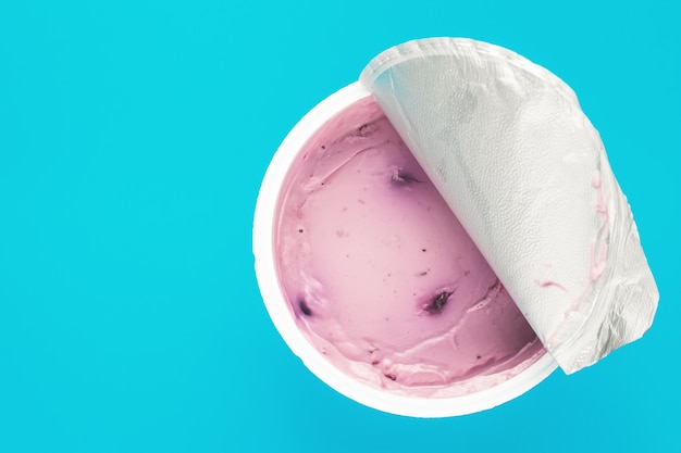 A pink yogurt with blueberry in an open plastic cup on blue background. Top view, text space.