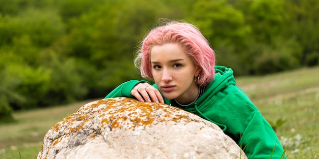 Pinkhaired girl sitting behind the Rock and looking at the camera