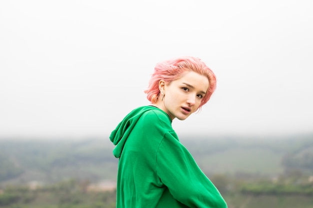 Pinkhaired girl wearing green hoodie and looking at the camera