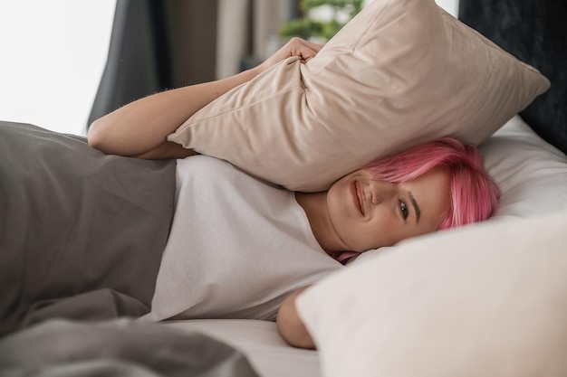 Pinkhaired young girl lying in bed and looking sleepy