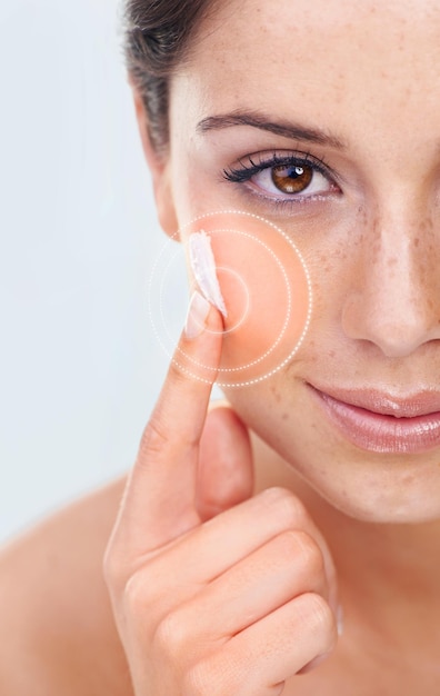 Pinpointing beauty. Studio portrait of a a beautiful young woman applying moisturizer to her cheek.