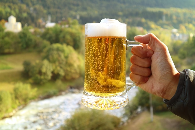 Pinta di birra in mano d'uomo contro sfocata vista sulla foresta pedemontana nella luce del sole serale