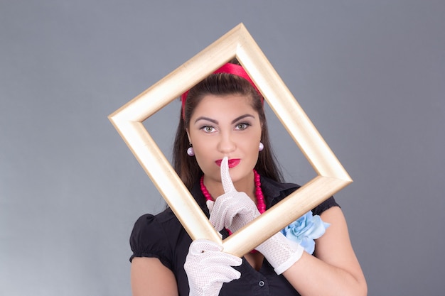 Pinup girl with a frame around her face and finger on lips over grey