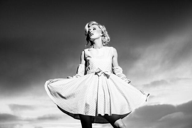 Pinup style woman in summer dress on dramatic sky fashionable young model in style dress fashion wom...