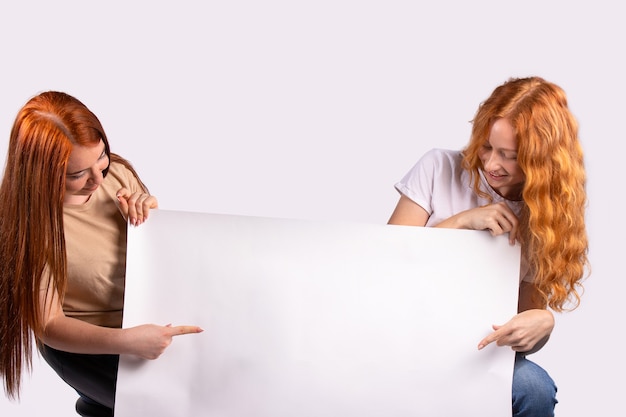 Photo pinup women showing forefinger hands on the blank banner photo for ad set of young caucasian pinup redhaired models on grey background with space for text