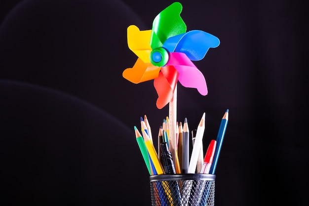 Pinwheel and pencils pot on stacked books, school supplies on white desk with blackboard texture in background.. Learning, education concept