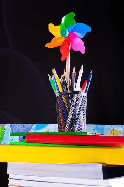 Pinwheel and pencils pot on stacked books, school supplies on white desk with blackboard texture in background.. Learning, education concept