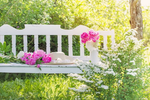 Pioen in kruik op witte houten bank in zomertuin