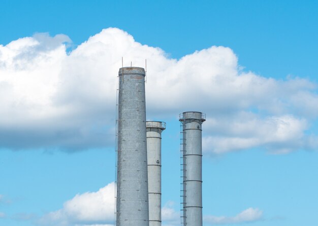 Pipes of an industrial enterprise against a blue sky with clouds. Chimney without smoke