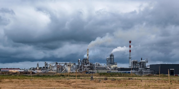 Pipes of woodworking enterprise plant sawmill against a gloomy\
gray sky air pollution concept panorama of industrial landscape\
environmental pollution waste of thermal power plant