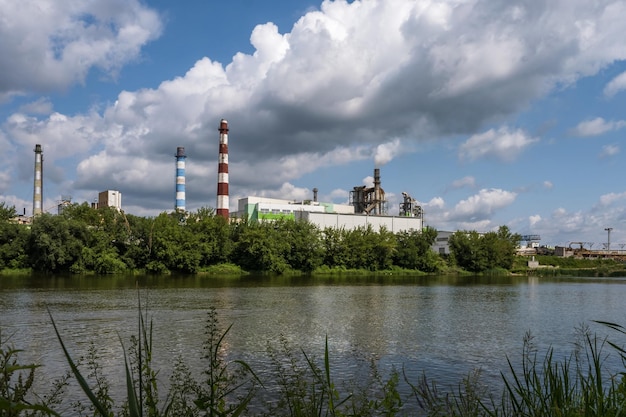 Pipes of woodworking enterprise plant sawmill near river air\
pollution concept industrial landscape environmental pollution\
waste of thermal power plant