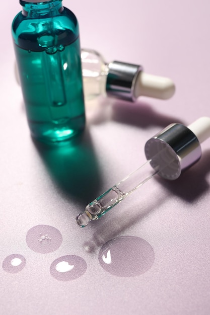pipette and bottles of moisturizing serum on light violet background closeup