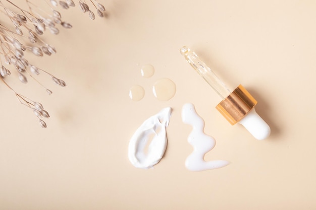Pipette and cosmetic smears with cream and drops of oil or serum on a beige background top view