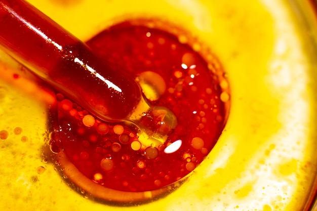피펫은 노란색 액체 박테리아 분자 오일의 표면에 작은 거품이 떠있는 크고 밝은 빨간색 거품을 관통합니다.