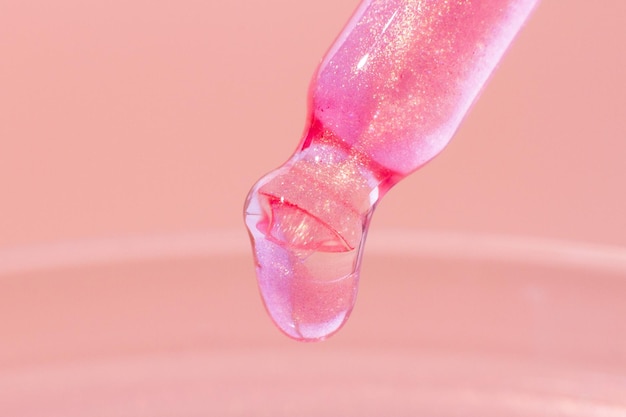 Пипетка с капающей розовой жидкостью Или жидким розовым золотом Крупным планом на розовом фоне Лабораторная химия медицина Косметические исследования блеск