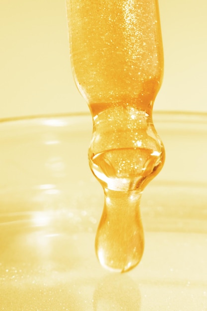 Pipette with dripping yellow liquid Or liquid gold Closeup On a golden background Laboratory chemistry medicine Cosmetic research shine