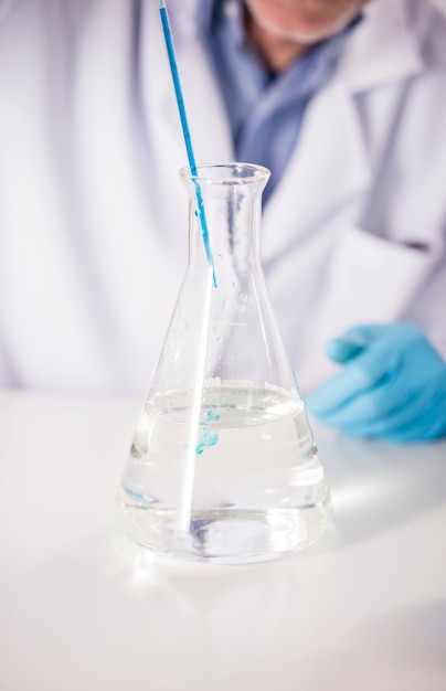 Пипетка с каплей химического над колбой научного стакана.