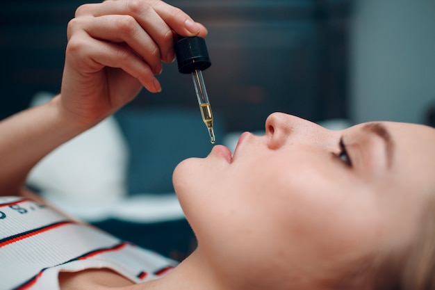 Pipette with liquid oil and young woman, close up portrait