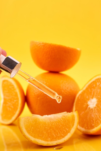 Pipette with orange essential oil over bottle and oranges on yellow background. Natural medicine concept. Aromatherapy