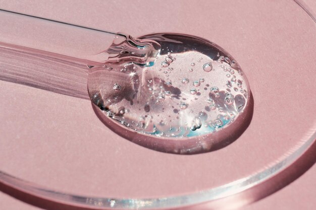 Pipette with sample of gels cosmetic product in petri dish on pink background hard shadows