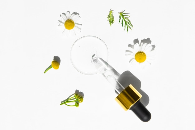 Pipette with transparent cosmetic liquid on a white background with chamomile flowers top view