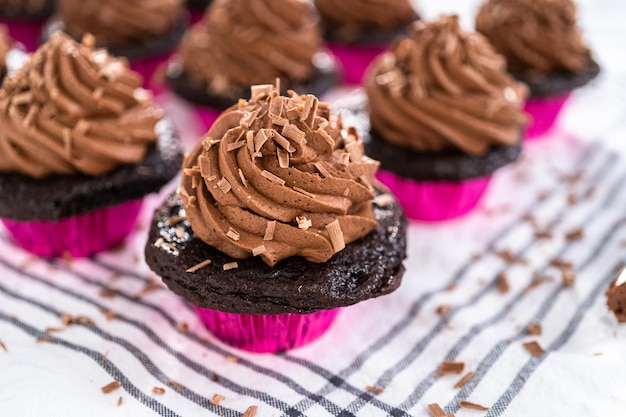 Photo piping chocolate ganache frosting on top of chocolate cupcakes.