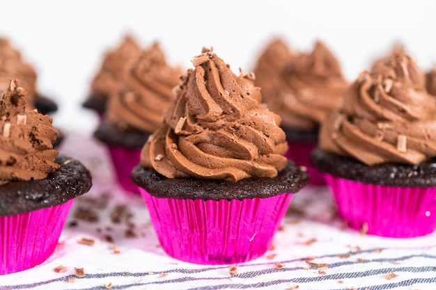 piping chocolate ganache frosting on top of chocolate cupcakes.