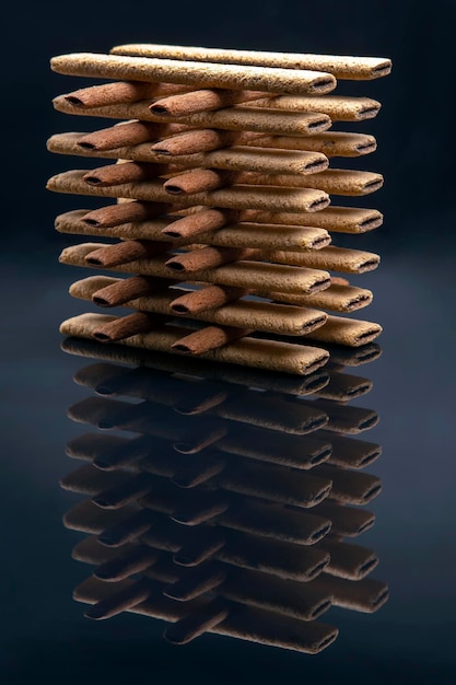 Foto piramide van zoete krokante cookie sticks met reflectie op donkere achtergrond. zoetwaren zoete producten. calorierijk voedsel voor thee en koffie