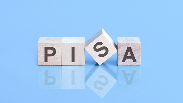 사진 pisa 단어는 비즈니스 개념인 파란색 테이블에 누워 있는 나무 큐브로 만들어졌습니다. pisa - program for international student assessment의 약자