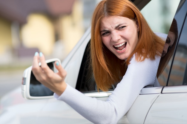 Photo pissed off displeased angry aggressive woman driving a car shouting at someone with middle finger gesture.