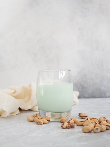 Pistachemelk in een glas met pistachenoten op een grijze achtergrond