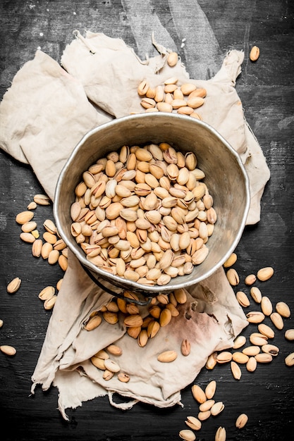 Pistachenoten in een oude emmer op stof op zwart bord.