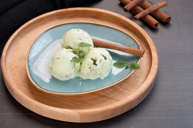 Фисташковое мороженое в черном вафельном рожке Орехово-зеленый десерт с палочками корицы на черном фоне