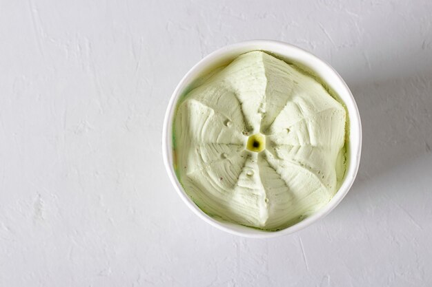 Pistachio ice cream in a paper cup on a light background. Takeaway food, top view. Copy space