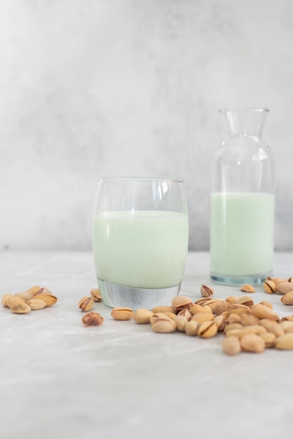 Pistachio milk in a glass and in a bottle with pistachios on a gray background