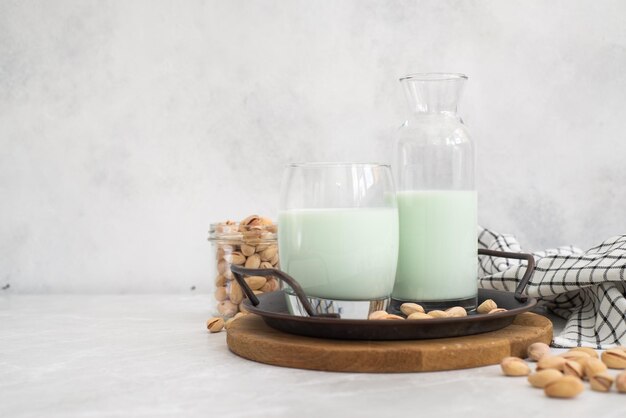 Pistachio milk in a glass and in a bottle with pistachios on a plate grey background