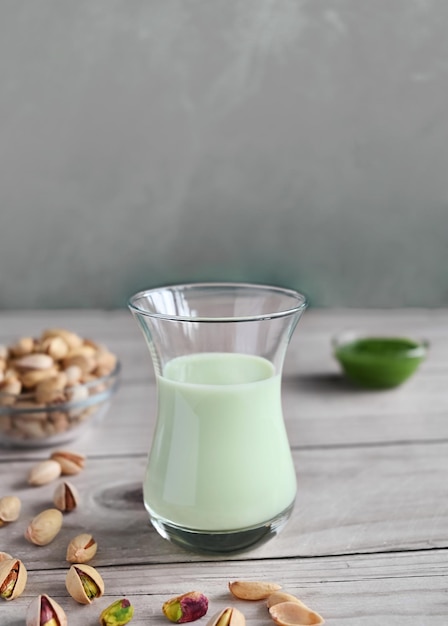 Pistachio milk in the glass and pistachio paste on the wooden background