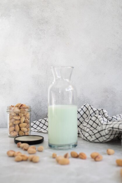 Pistachio milk in a glass with pistachios on a grey plate and grey background