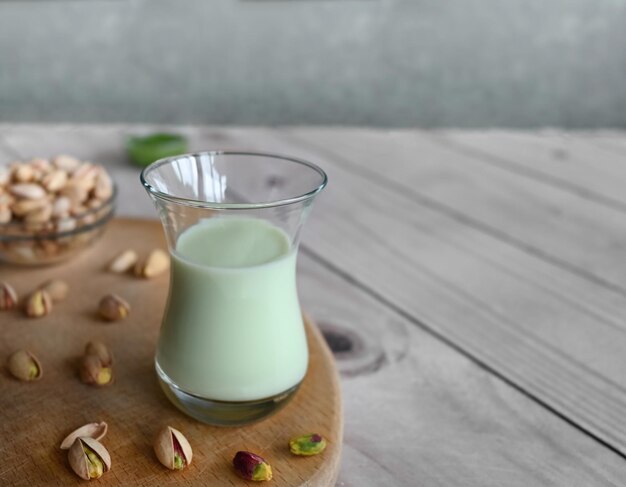 Фото Фисташковое молоко в стакане на деревянном фоне. это молоко является отличным источником антиоксидантов, фитостеролов и полезных для сердца жиров.
