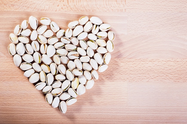 Pistachio nuts forming a heart-shape on wooden floor background