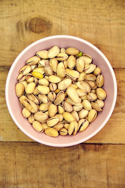 Pistachio nuts in pink bowl on old wooden table background Top view