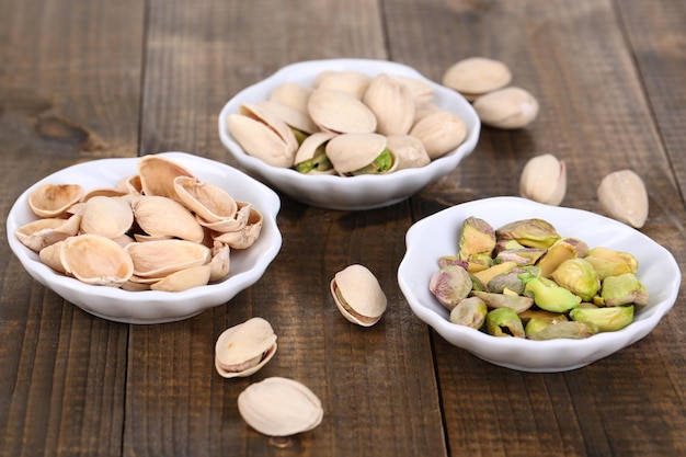 Pistachio nuts in small bowls on wooden background